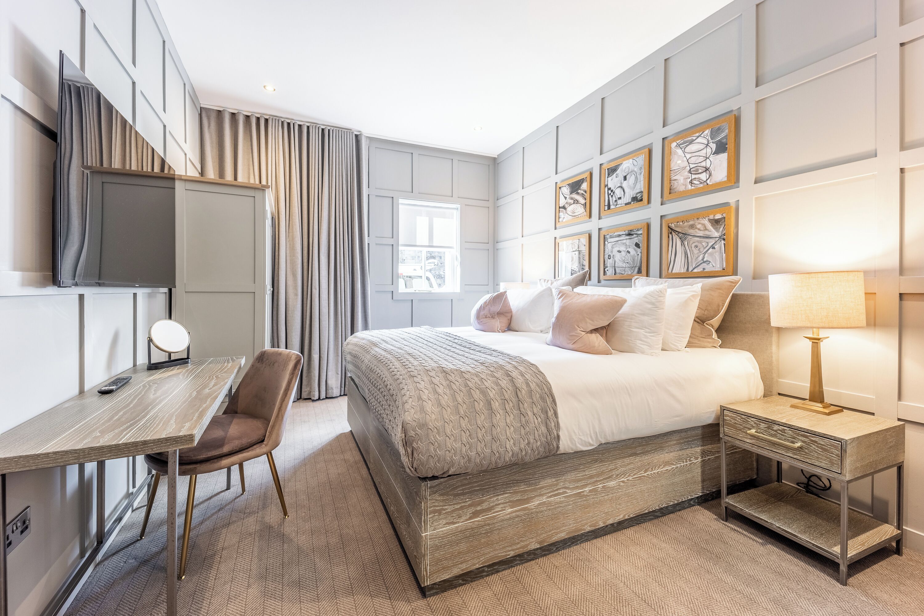Una habitación de hotel moderna con cama, escritorio, silla, televisor y obras de arte en las paredes.