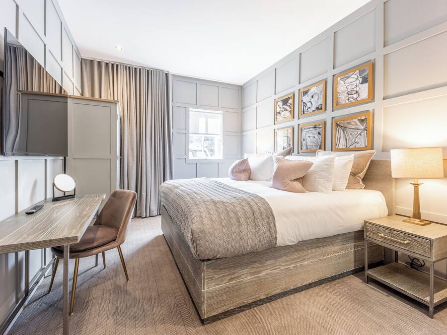Una habitación de hotel moderna con cama, escritorio, silla, televisor y obras de arte en las paredes.