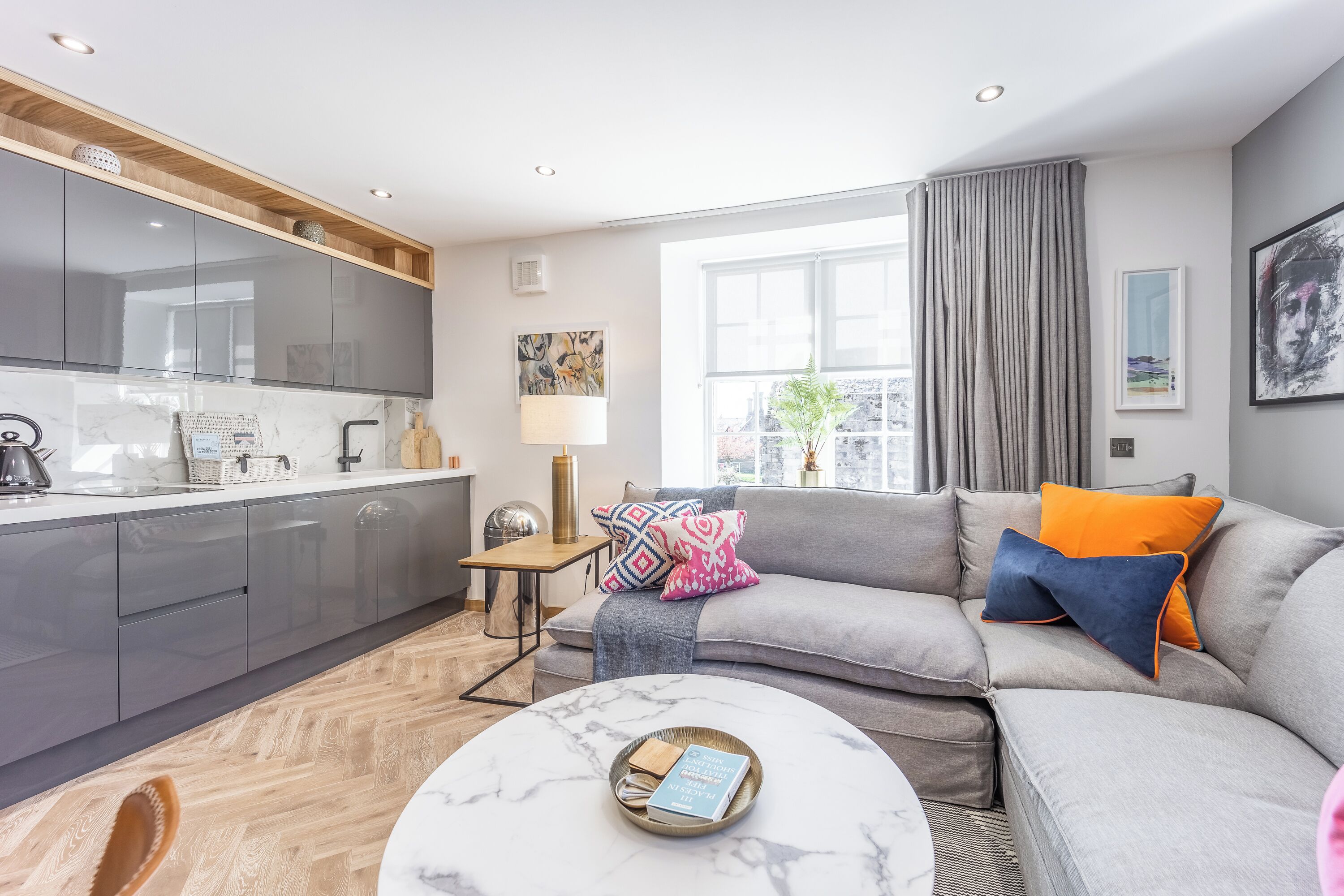 Ein modernes Wohnzimmer mit einem grauen Sofa, einem Couchtisch und einer Küchenzeile mit grauen Schränken und einer Marmorarbeitsplatte.