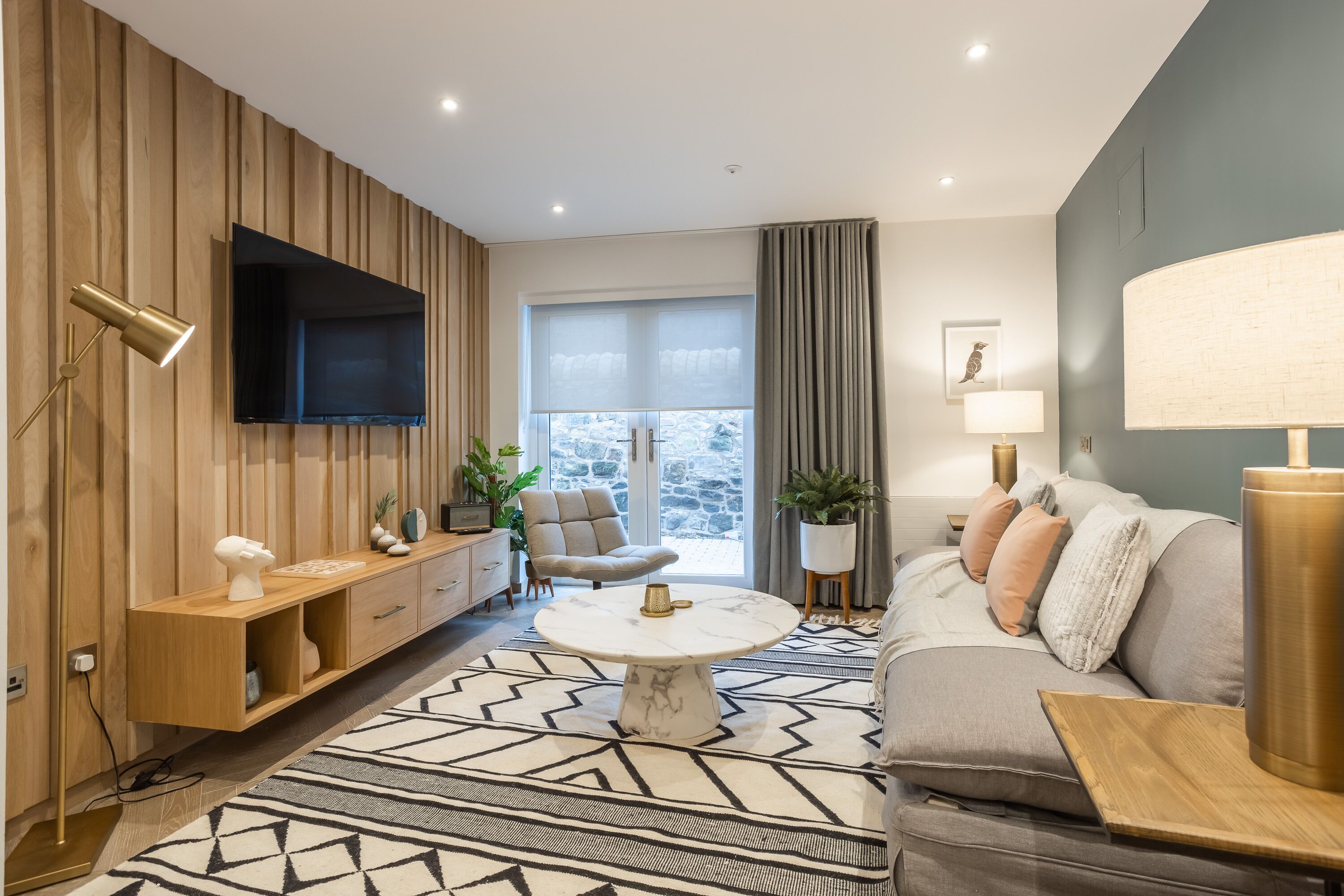 A modern living room with a wooden panel wall, a flat-screen TV, a round coffee table, a sofa, and a patterned rug.