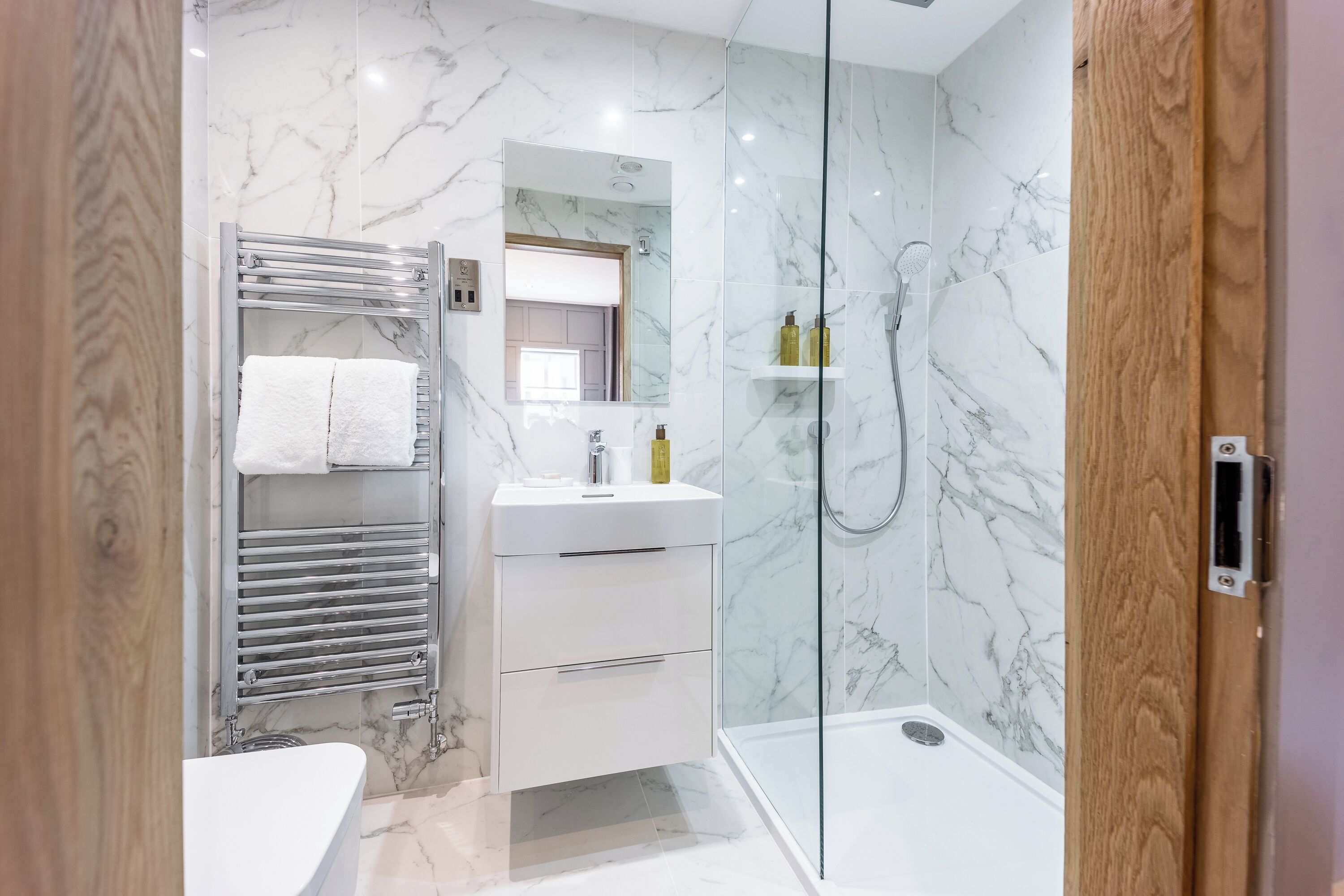 A modern bathroom with a glass shower enclosure, a white vanity with a mirror, and a towel rack with two towels.