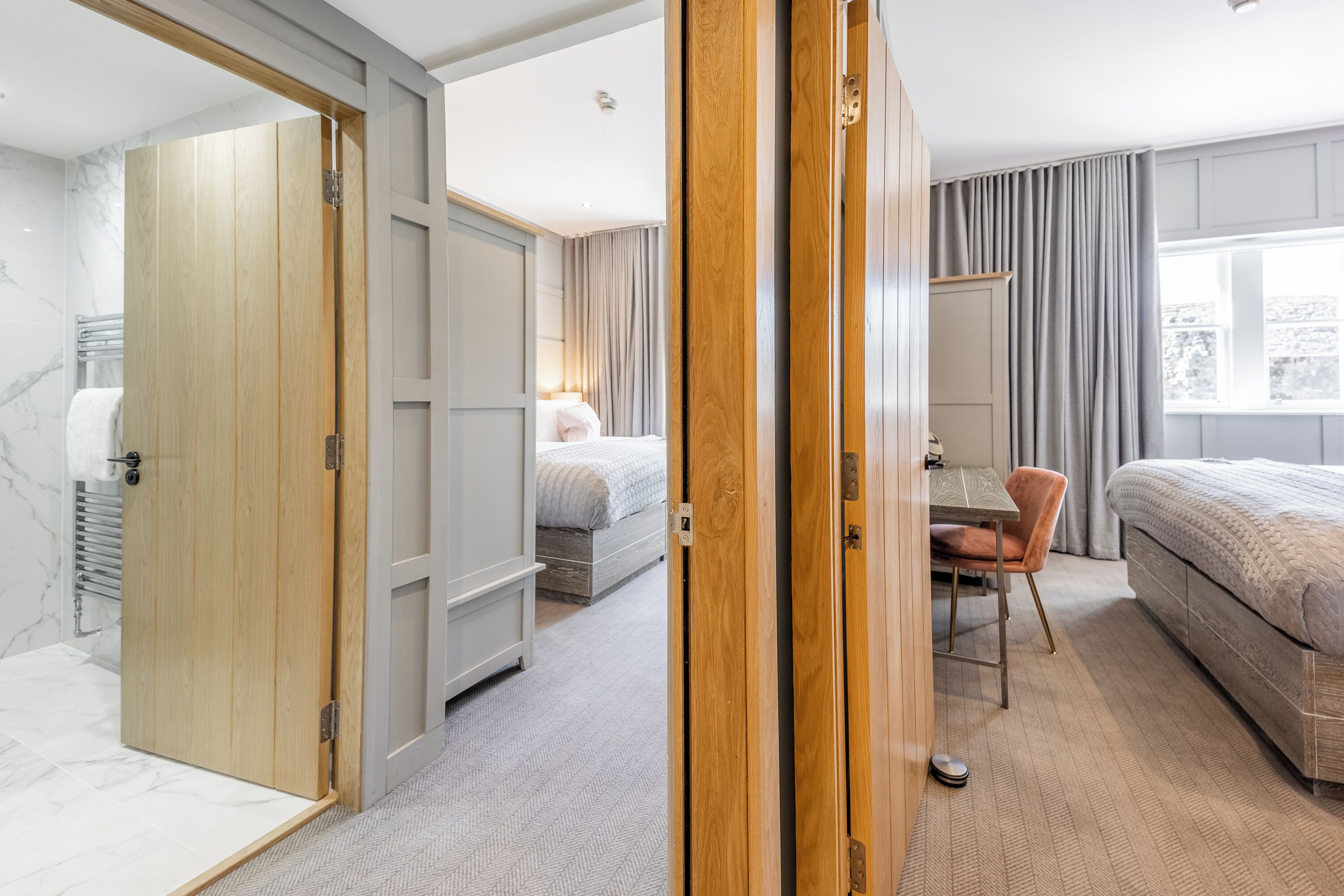 Quarto de hotel com porta de madeira, uma cama, escrivaninha e cadeira.