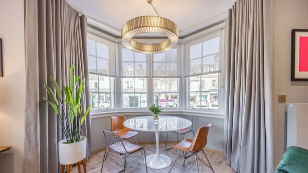 Une pièce moderne avec une table ronde, quatre chaises, une plante en pot et de grandes fenêtres donnant sur la ville.