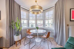 A modern room with a round table, four chairs, a potted plant, and large windows offering a city view.