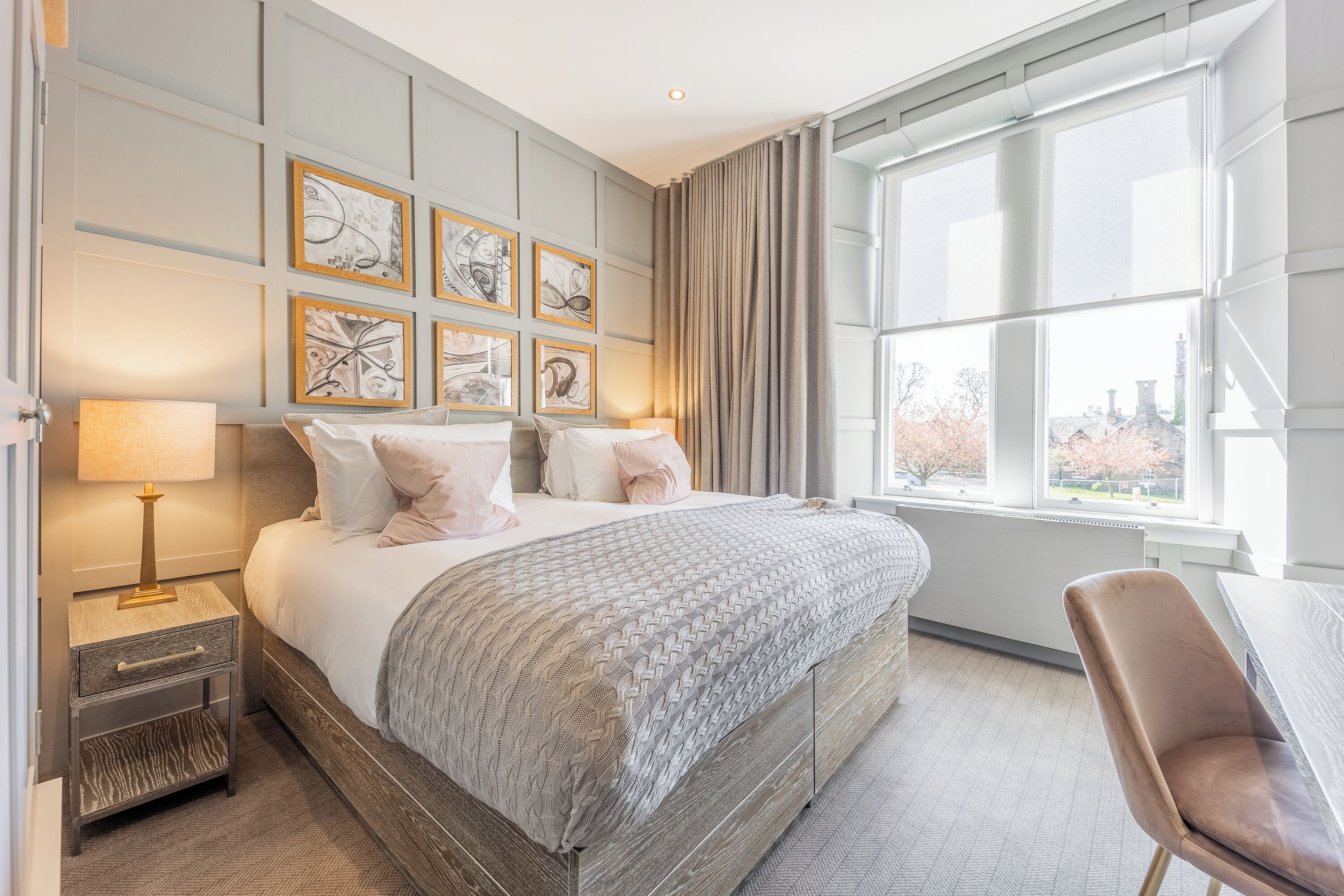 Een moderne hotelkamer met een groot bed, een bureau en uitzicht op de stad door grote ramen.