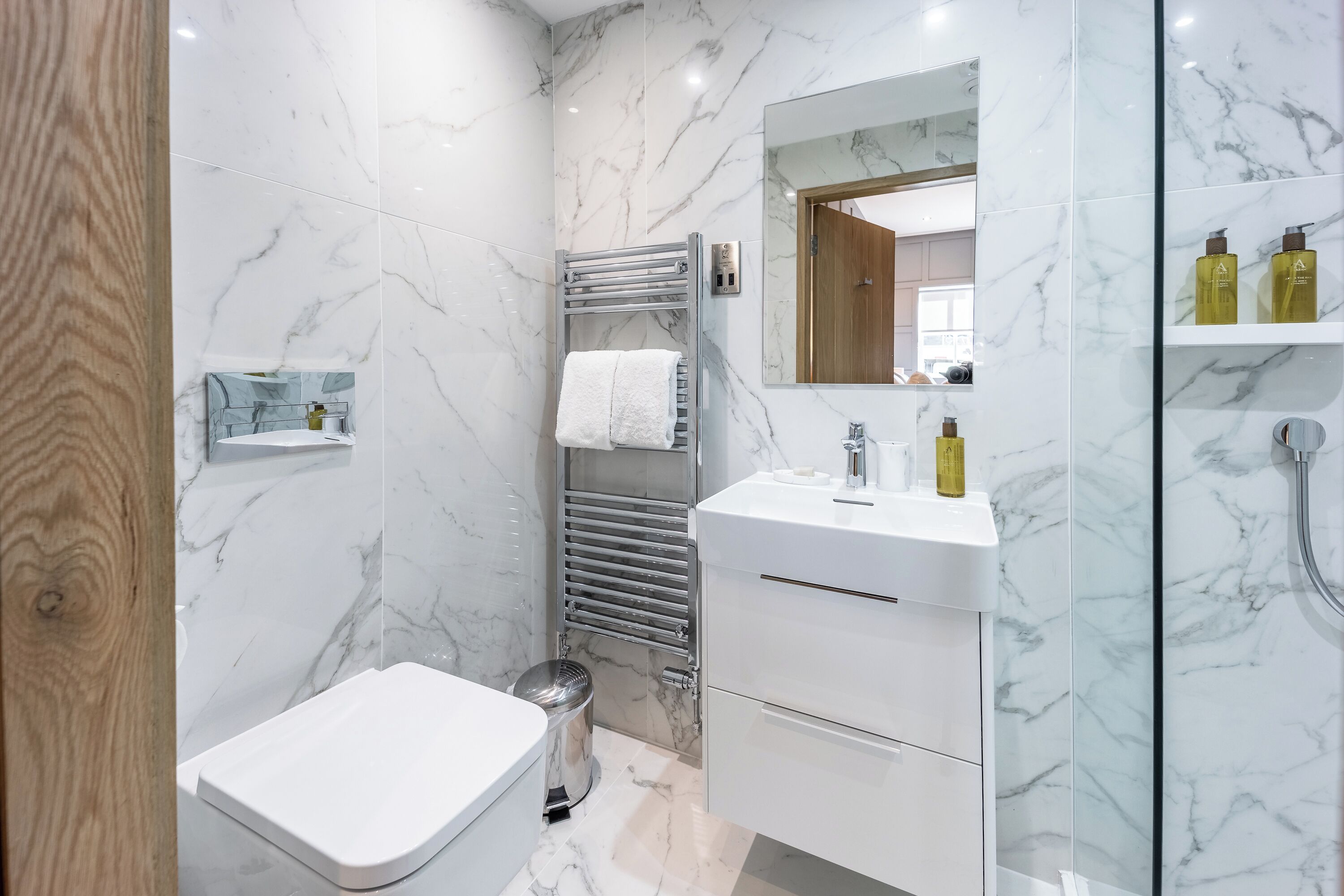Un bagno moderno con pavimento in marmo, un water bianco, box doccia in vetro e un mobile vanitario con specchio e scaffali.