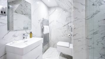 A modern bathroom with a marble floor, a white sink, a toilet, and a glass-enclosed shower area.