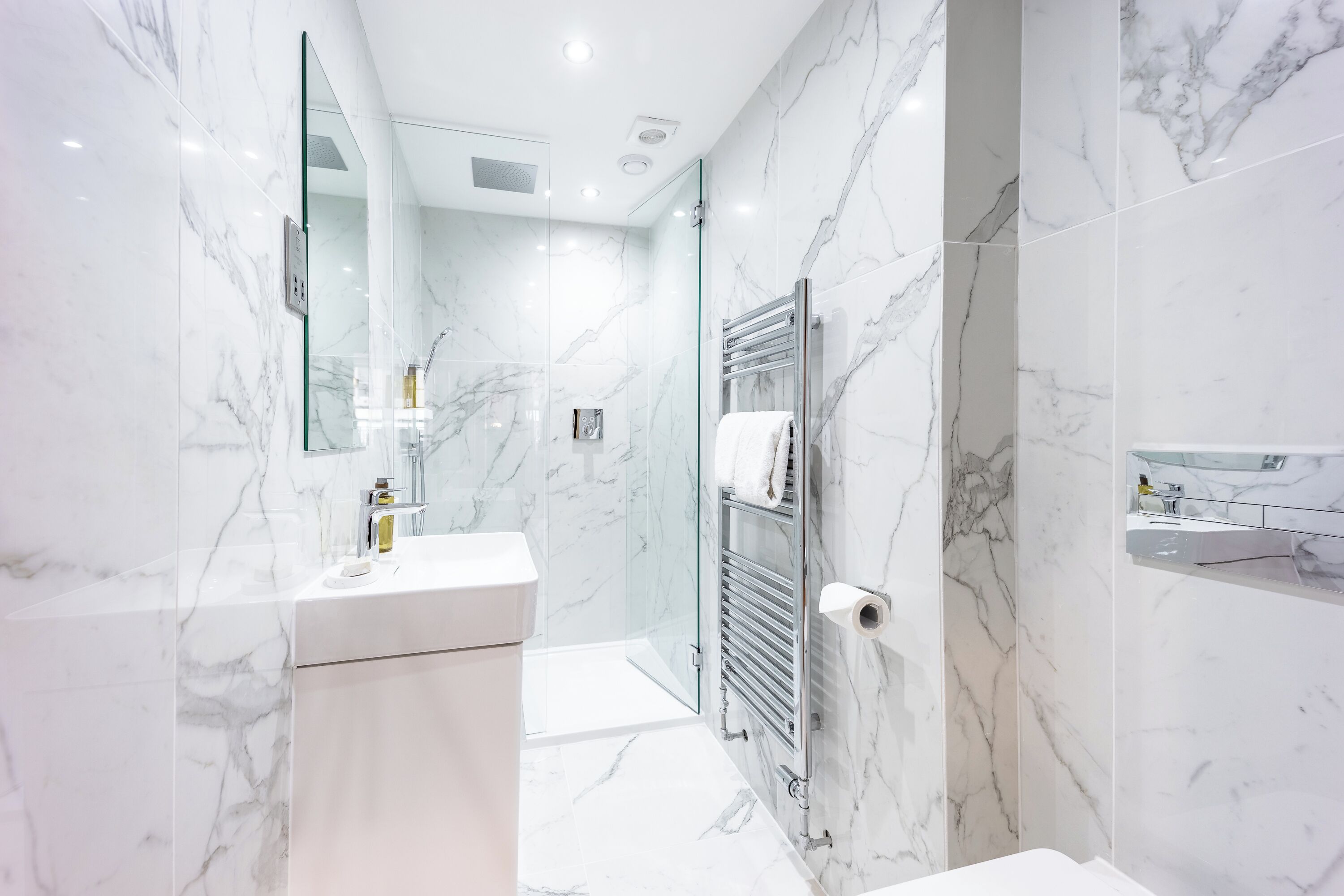 A modern bathroom with marble walls, a glass shower enclosure, and a white vanity.