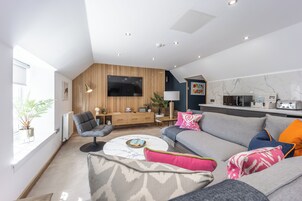 A modern living room with a grey sofa, a round coffee table, and a TV mounted on a wooden wall.