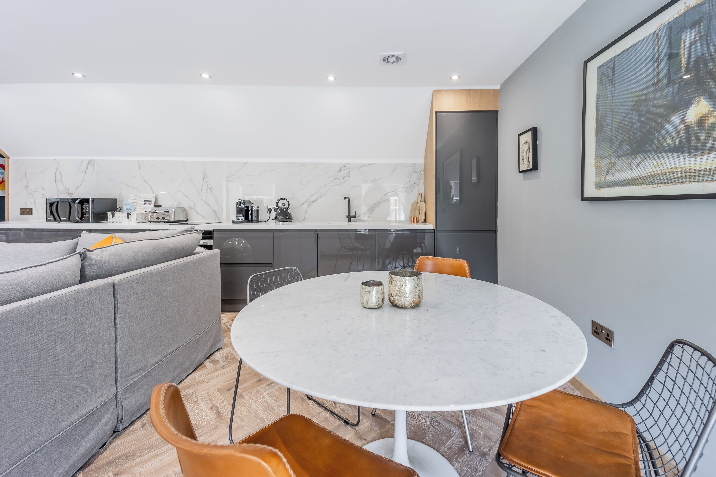 A modern kitchen with a marble backsplash, a round dining table, and a gray sofa.