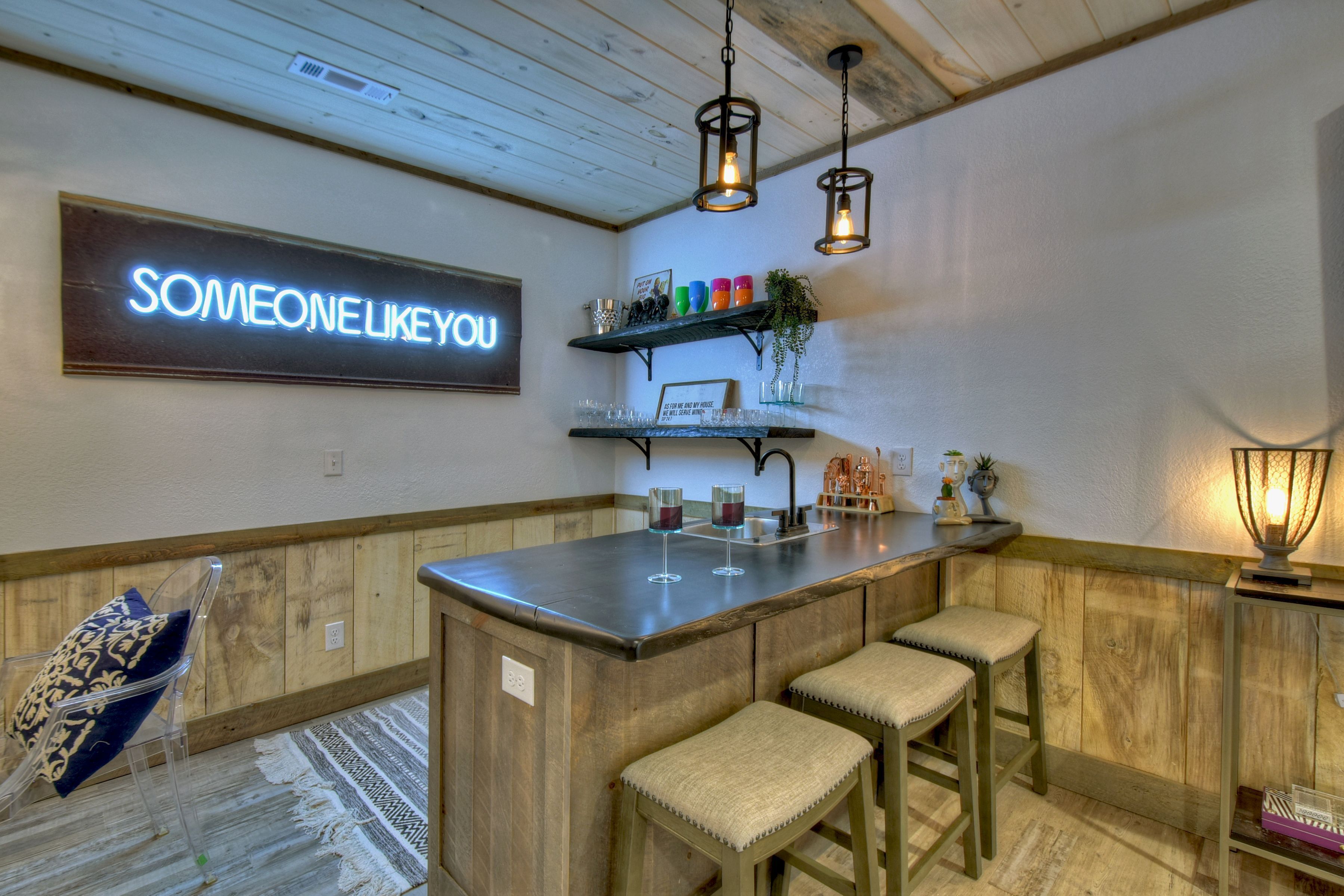 A kitchen with a bar area, a neon sign, and a wooden floor.