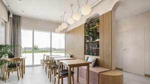 Un comedor moderno con mesas y sillas de madera, un banco de madera redondo y una estantería con plantas.
