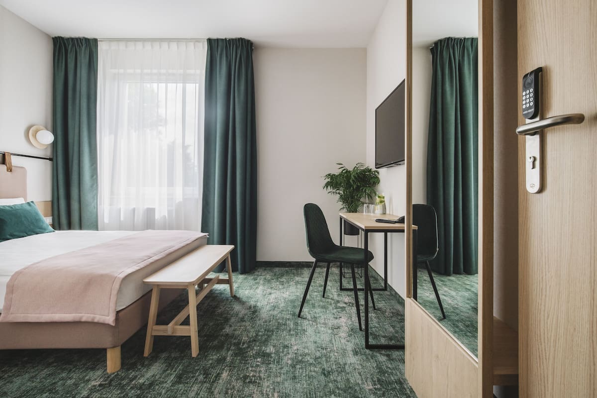 Een hotelkamer met een bed, bureau, stoel en een grote spiegel.