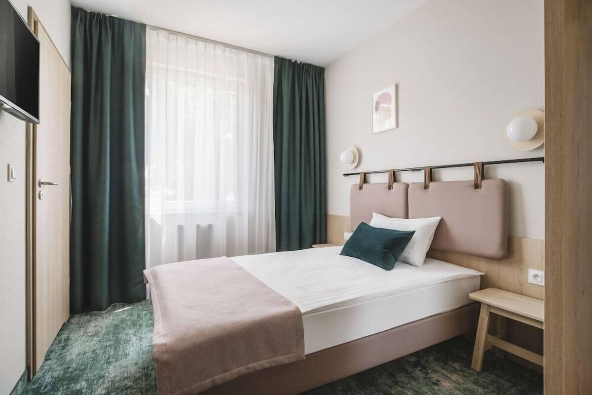 Een hotelkamer met een bed, nachtkastje, televisie en raam met gordijnen.