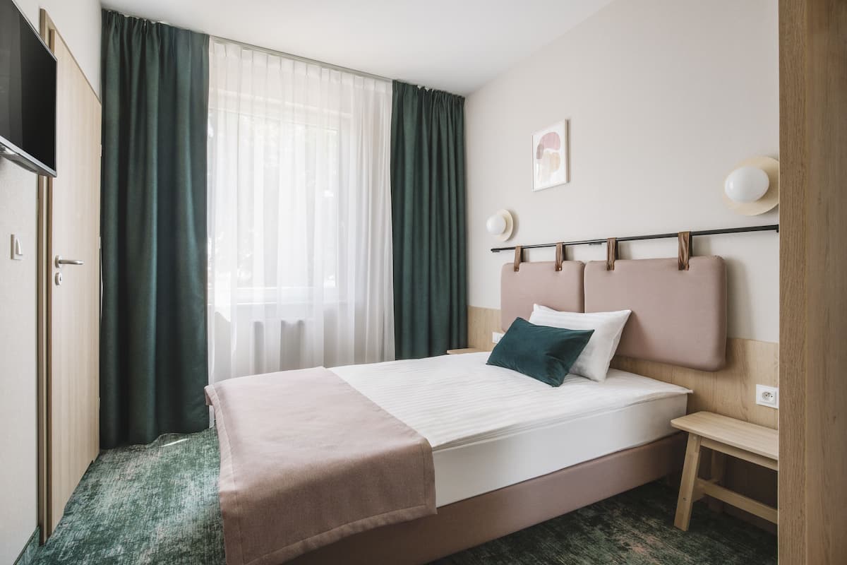 Een hotelkamer met een bed, nachtkastje, televisie en raam met gordijnen.