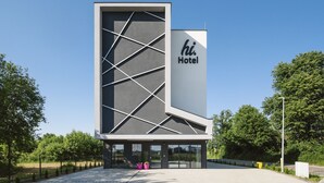 Un moderno edificio de hotel con un llamativo letrero 'hi Hotel', que presenta una fachada geométrica y una entrada espaciosa.