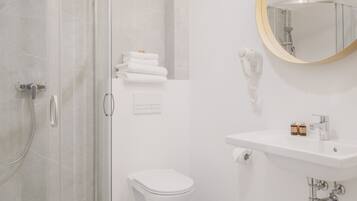 Un baño moderno con cabina de ducha de vidrio, inodoro, lavabo con espejo y barra para toallas.