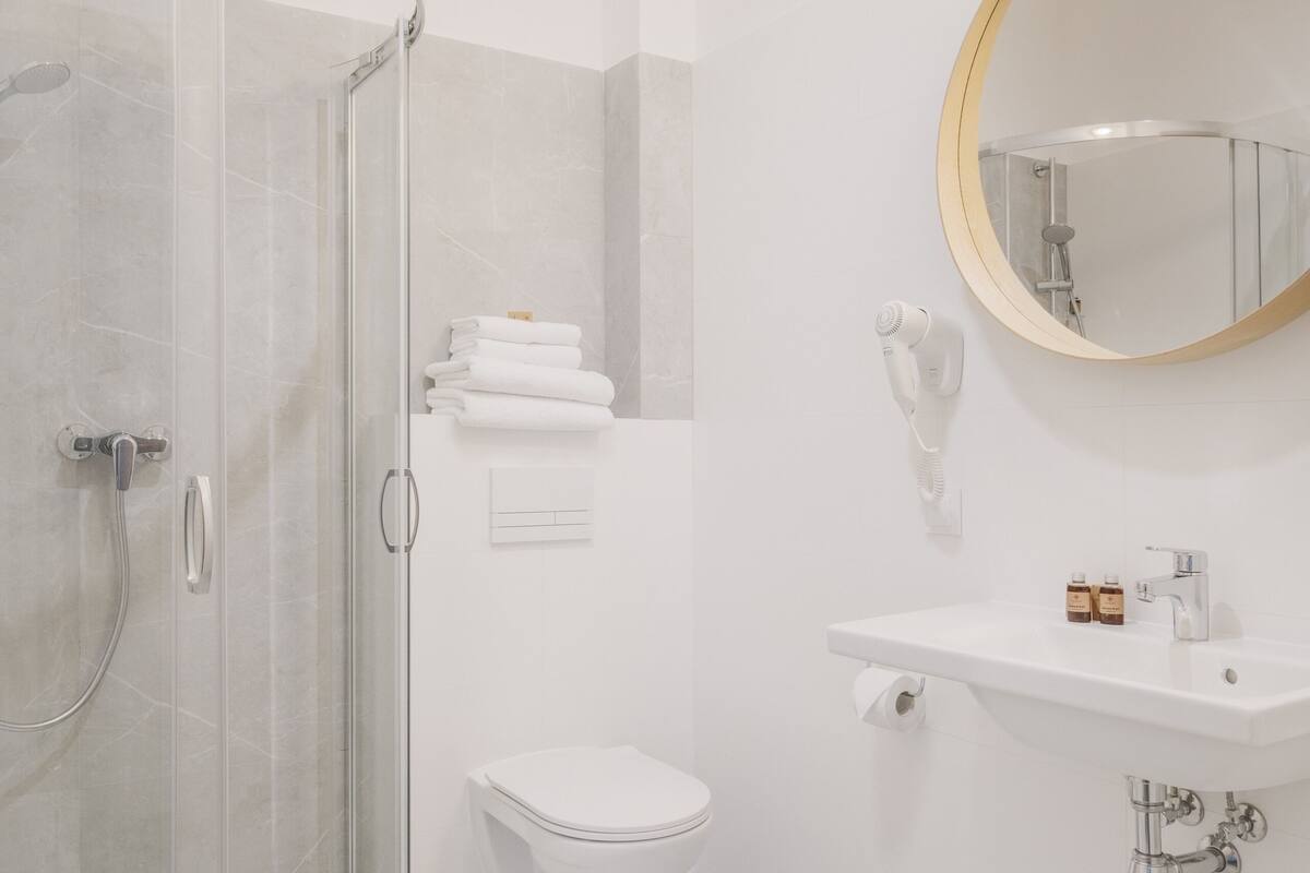 Een moderne badkamer met een douchecabine van glas, een toilet, een wastafel met spiegel en een handdoekrek.