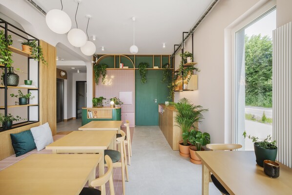 Un intérieur moderne avec des tables et des chaises en bois, un coin cuisine et diverses plantes en pot.