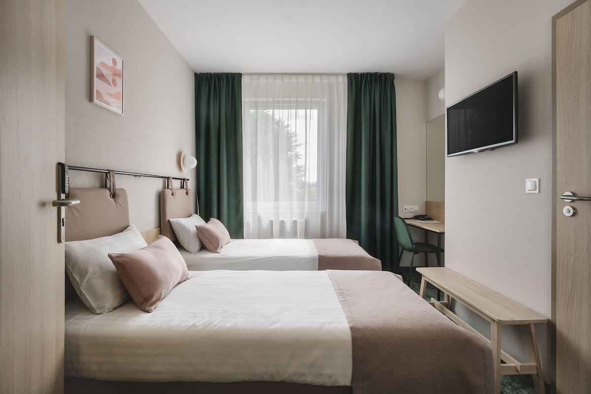 Een hotelkamer met twee bedden, een bureau, een televisie en een raam met gordijnen.