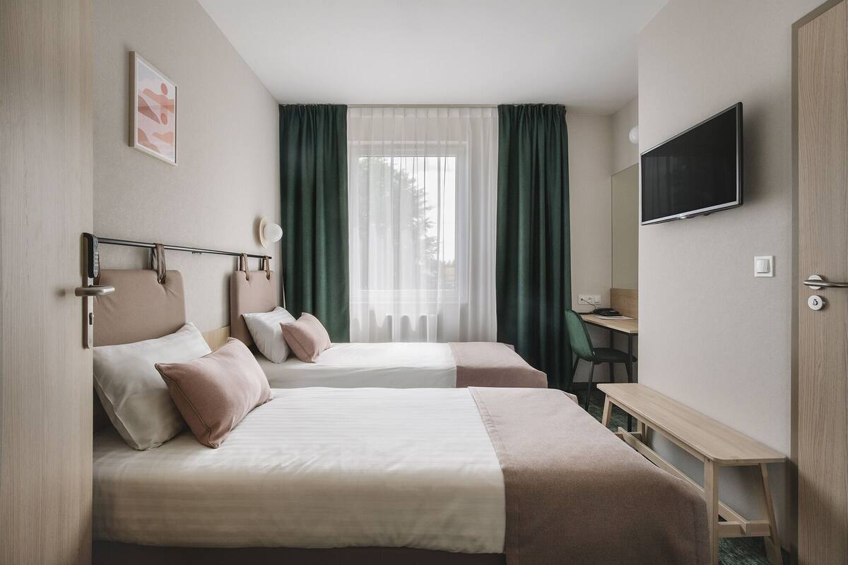 Een hotelkamer met twee bedden, een bureau, een televisie en een raam met gordijnen.