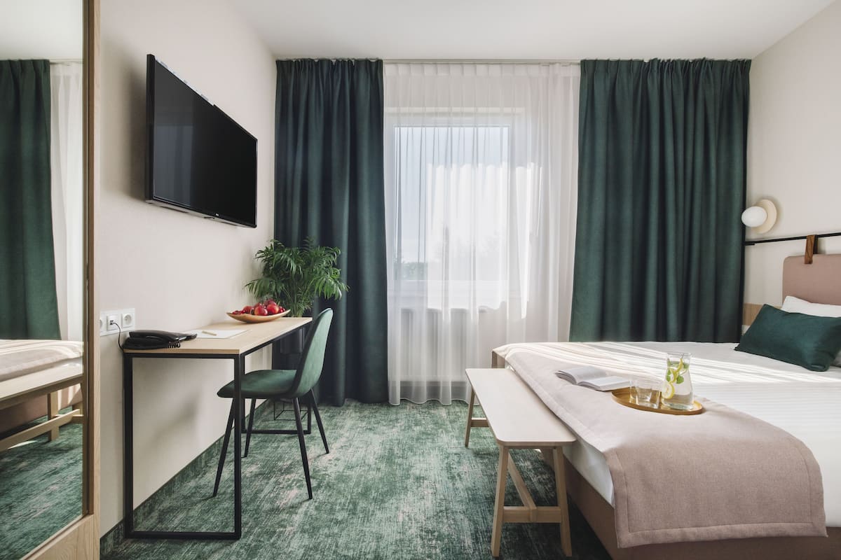 Een hotelkamer met een bed, een bureau met stoel, een televisie en een raam met gordijnen.