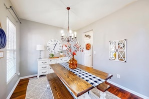 A dining area with a wooden table, a chandelier, a clock, and a door with a wreath.