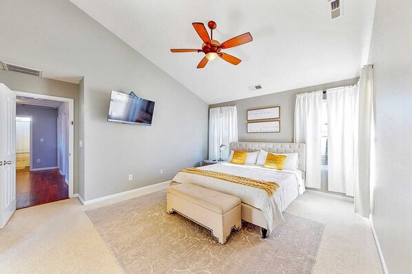 A bedroom with a bed, a ceiling fan, a TV, and a window with curtains.