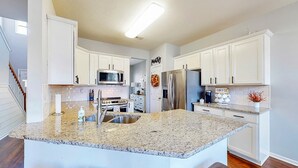 Una cocina moderna con gabinetes blancos, encimeras de granito, electrodomésticos de acero inoxidable y una isla central con taburetes de bar.