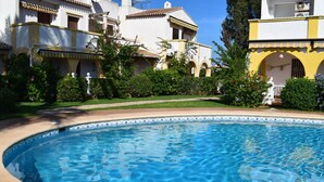 Ein Swimmingpool, umgeben von einem gepflegten Garten und einem Gebäude mit gelber Fassade.