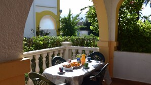 Eine Terrasse im Freien mit einem für das Frühstück gedeckten Tisch, umgeben von Stühlen und einem weißen Geländer.
