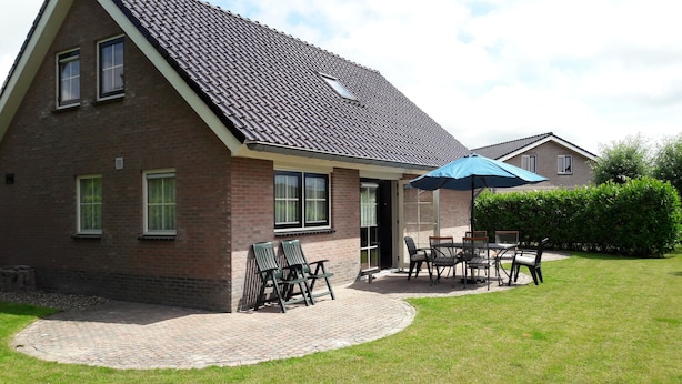 Ein zweistöckiges Ziegelhaus mit einem Ziegeldach, einer Terrasse mit Gartenmöbeln und einem gepflegten Rasen.