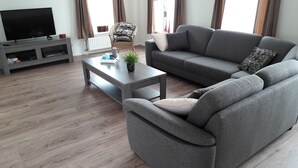 Ein modernes Wohnzimmer mit einem grauen Sofa, einem Couchtisch mit einer Pflanze und einem Fernseher auf einem Holzboden.