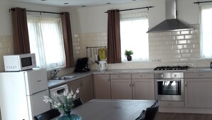 Eine moderne Küche mit Essbereich, weißen Schränken, Edelstahlgeräten und einem großen Fenster mit Vorhängen.