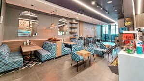 Een modern café met blauw gestreept zitmeubilair, een balie met lekkernijen en een groot raam met uitzicht.