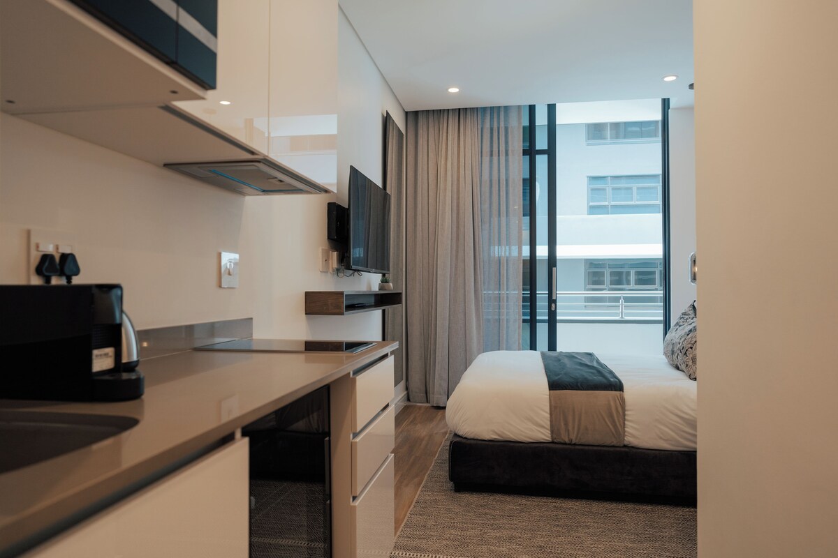 Una habitación de hotel moderna con una cama, un escritorio, un televisor y vistas a la ciudad.