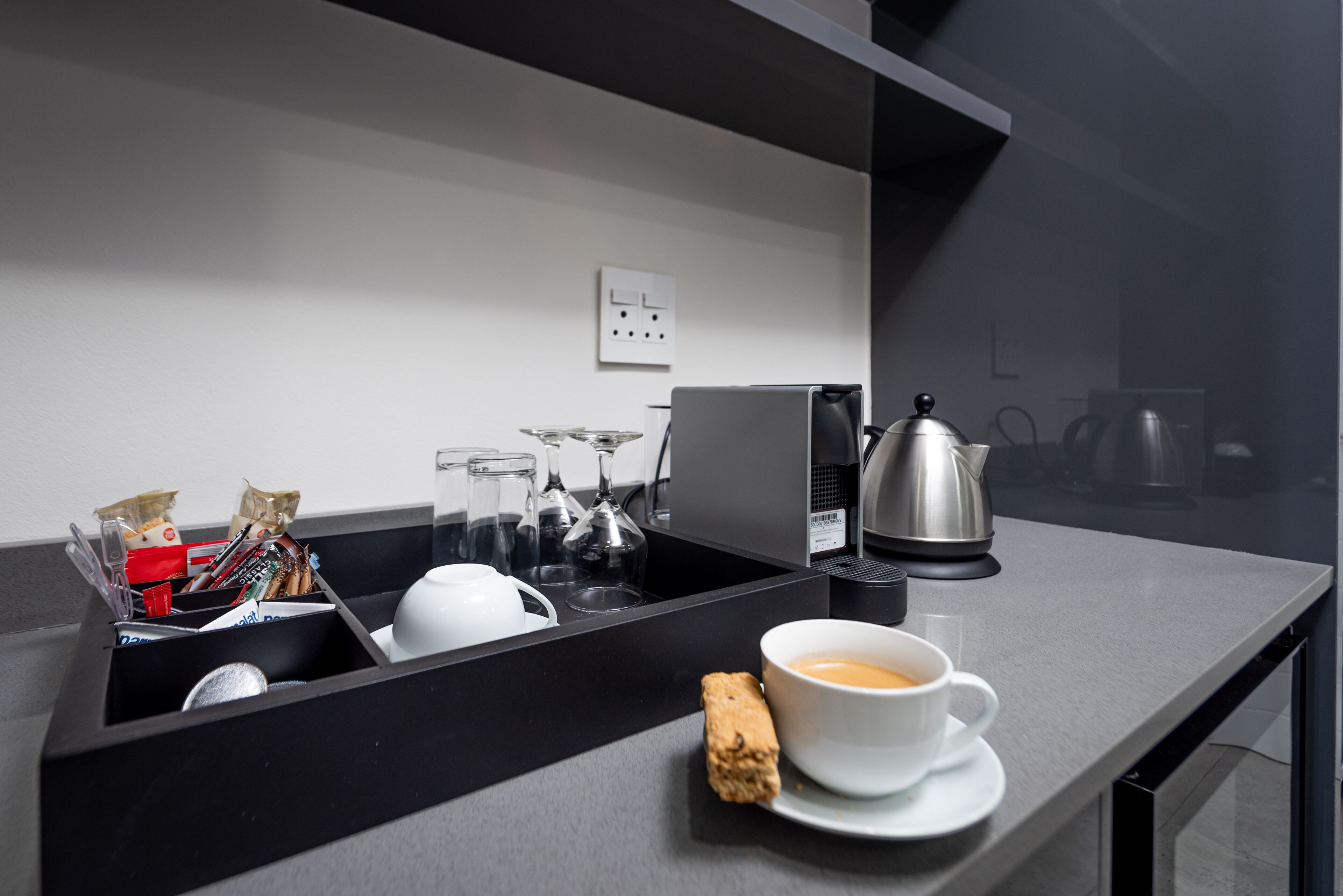 Eine moderne Küche mit schwarzem Arbeitsplatz, einer Kaffeemaschine, einem Wasserkocher und einer Tasse Kaffee.