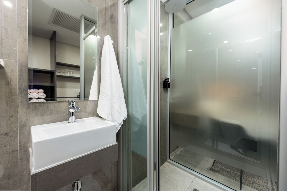 Un baño moderno con un lavabo blanco, cabina de ducha de vidrio y un espejo con una toalla colgada.
