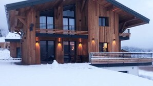 A modern wooden cabin with a balcony, large windows, and a snow-covered ground. - Chalet nestled above the slopes at Les Houches (Les Houches)