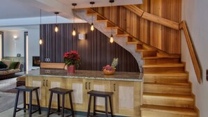 A modern kitchen with a wooden staircase, a central island with stools, and pendant lighting. - Chalet nestled above the slopes at Les Houches (Les Houches)