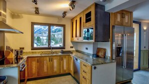 A modern kitchen with wooden cabinets, a stainless steel refrigerator, and a window with a mountain view. - Chalet nestled above the slopes at Les Houches (Les Houches)