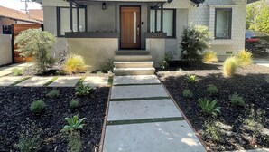 A two-story house with a brick facade, a front door, and a small front yard with plants and a pathway. - Beautiful 2 Bedroom Home in Santa Monica (Santa Monica)