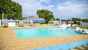 Una piscina rettangolare con bordo piastrellato, circondata da lettini e un'area salotto coperta.
