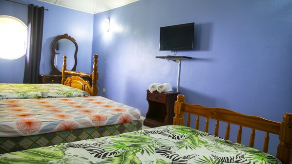 A room with two beds, a wooden headboard, a television mounted on the wall, and a small table with towels. - Maranatha Villa (Discovery Bay)