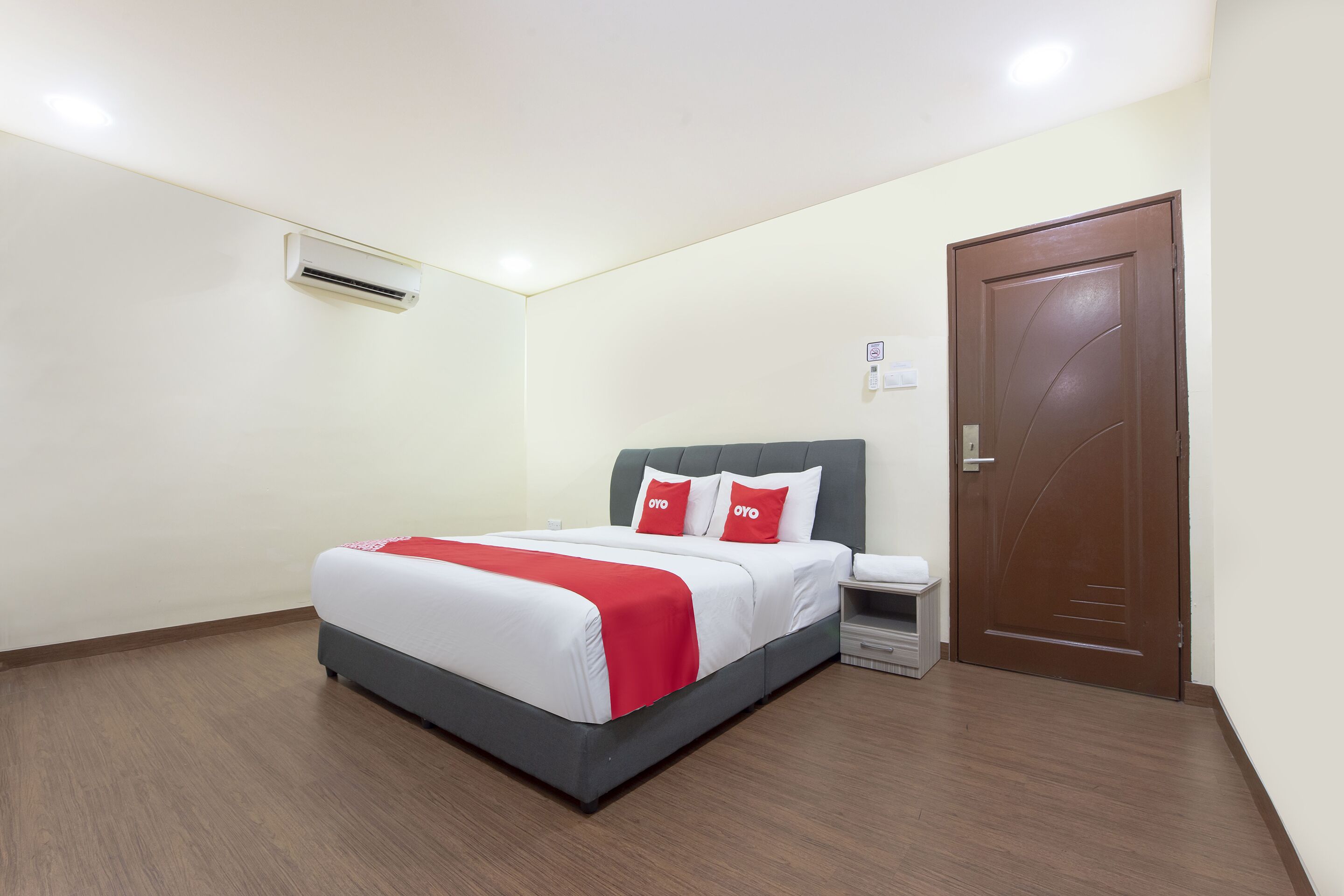 A hotel room with a bed, a nightstand, a door, and an air conditioning unit.