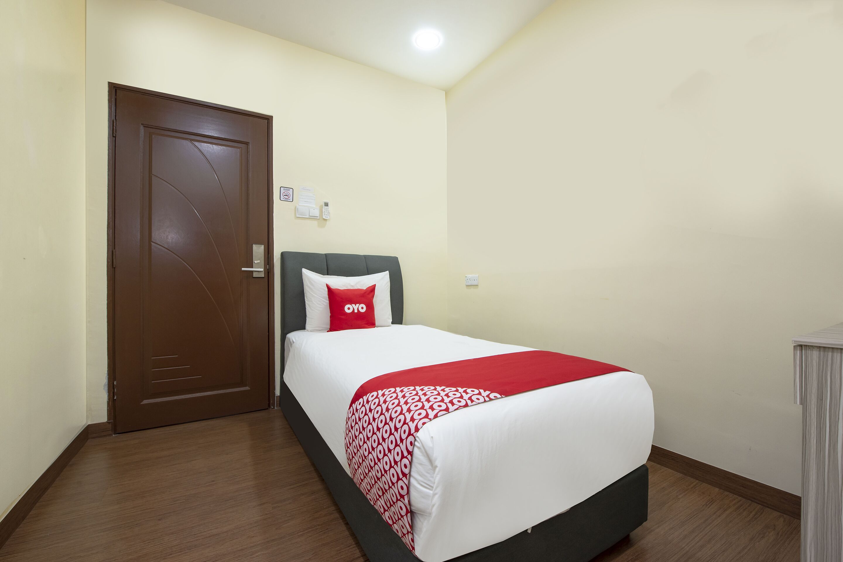 A hotel room with a single bed, a wooden floor, a door, and a small desk.