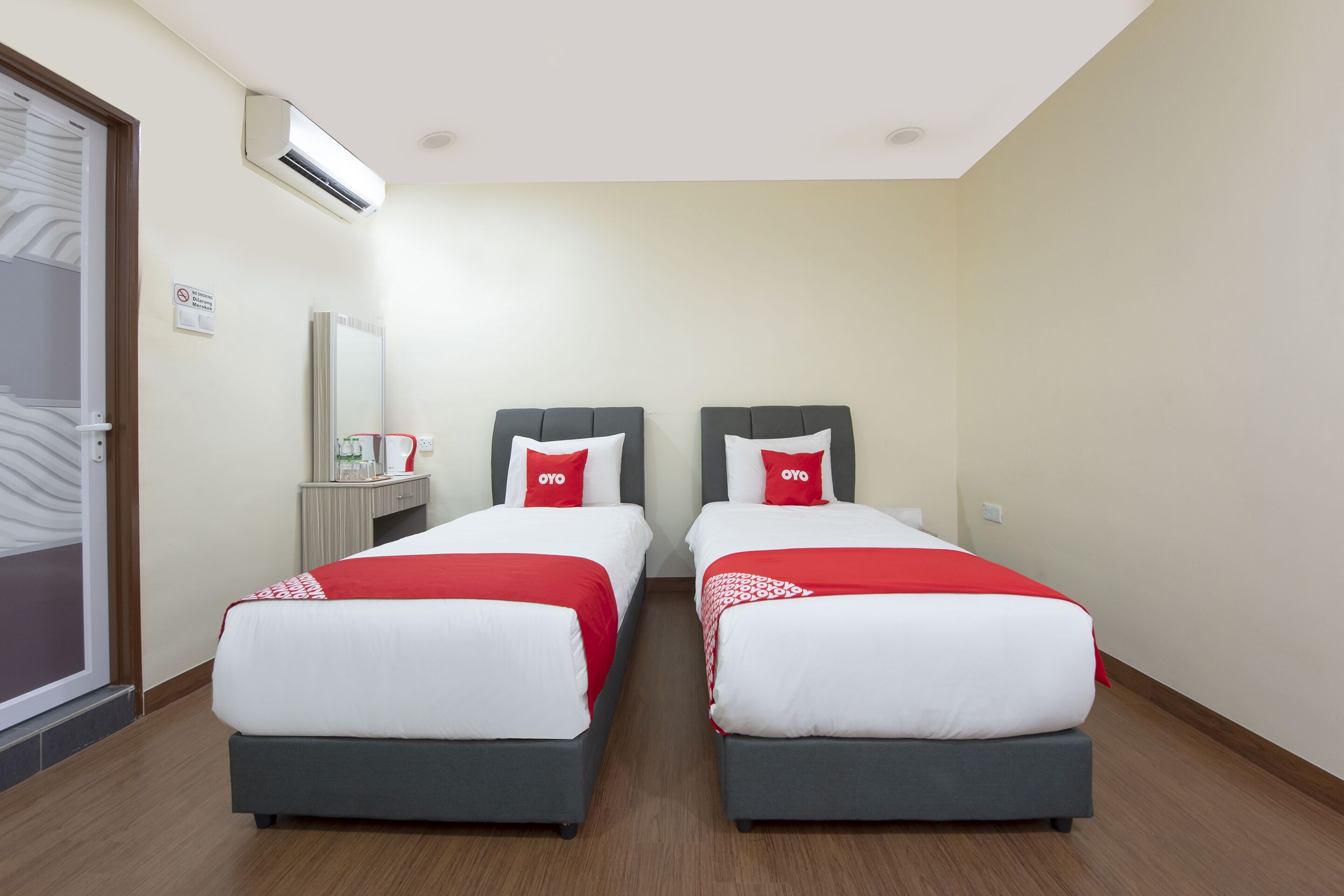 Een hotelkamer met twee bedden, elk met een rode en witte spreideken, en een klein tafeltje met een spiegel en een rode lamp.