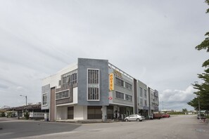Un hotel moderno con un llamativo letrero 'HOTEL', entrada a un garaje y un estacionamiento con varios vehículos.