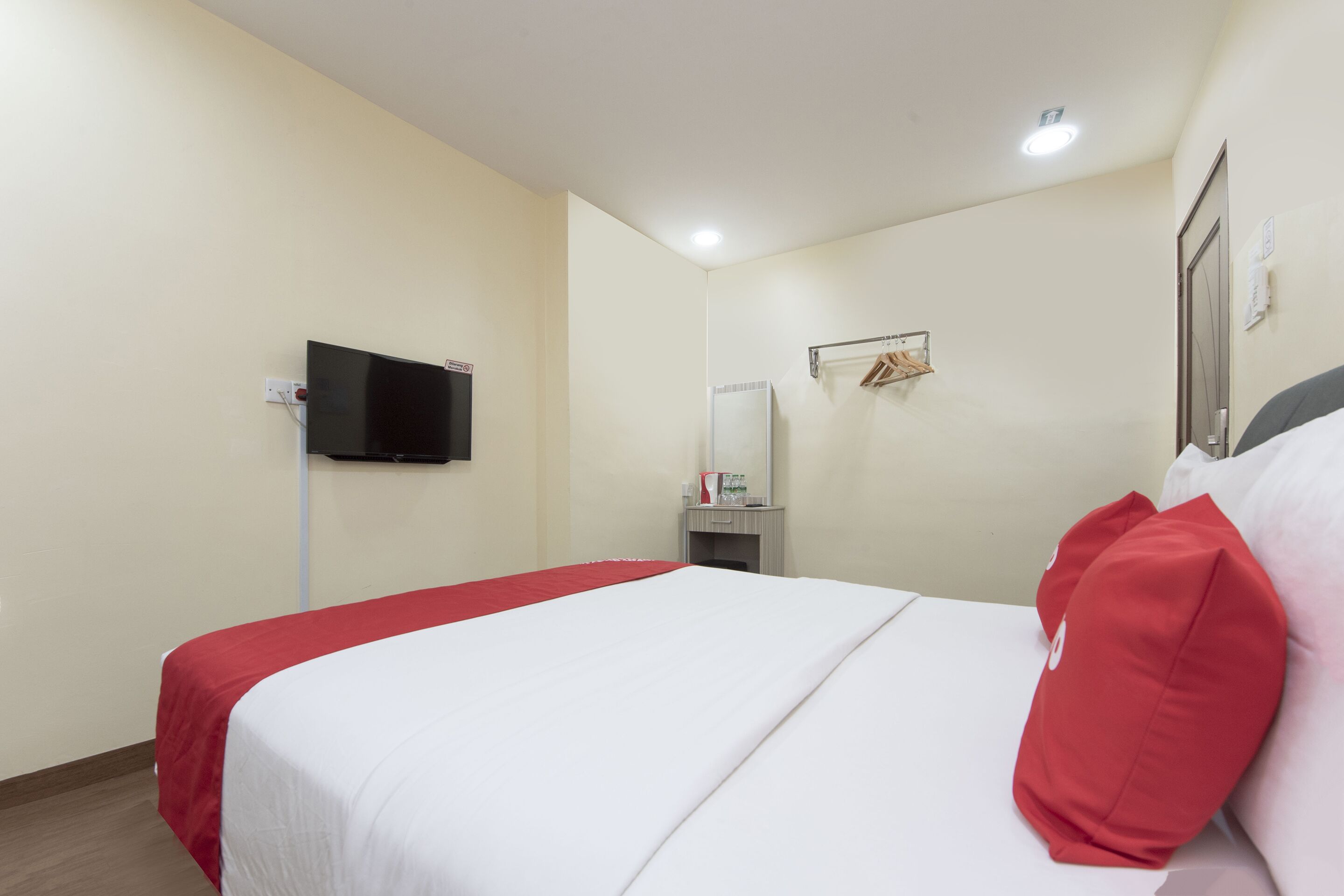 A hotel room with a bed, a television mounted on the wall, a mirror, and a small table with a kettle.