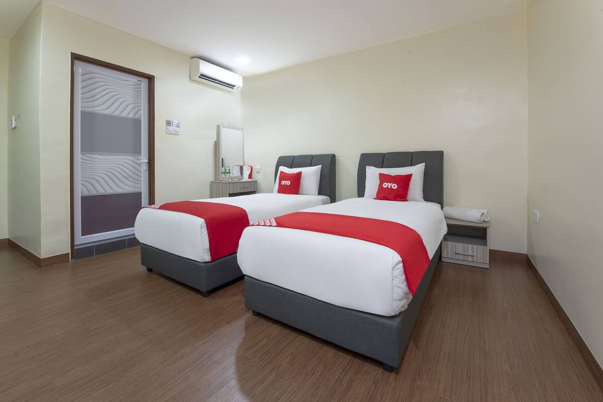 Ein Hotelzimmer mit zwei Betten, jeweils mit roter und weißer Bettwäsche, einem kleinen Nachttisch, einem Spiegel und einem Kleiderschrank.